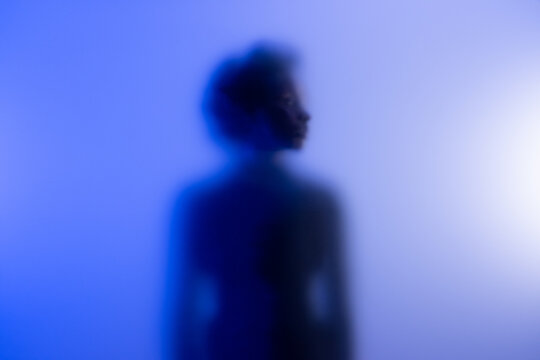 Young black woman standing behind frost glass in studio. and looking away. 