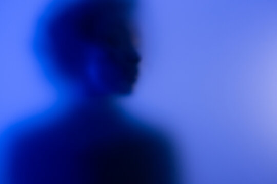 Blurry portrait of anonymous black woman behind frosted glass in blue and purple light at studio. 
