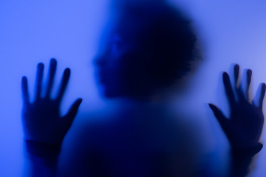 Young black woman behind the frost glass is seeking for help in her emotional confinement. 