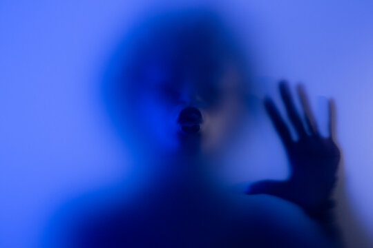 Anonymous black woman kissing frosted glass in studio blue light