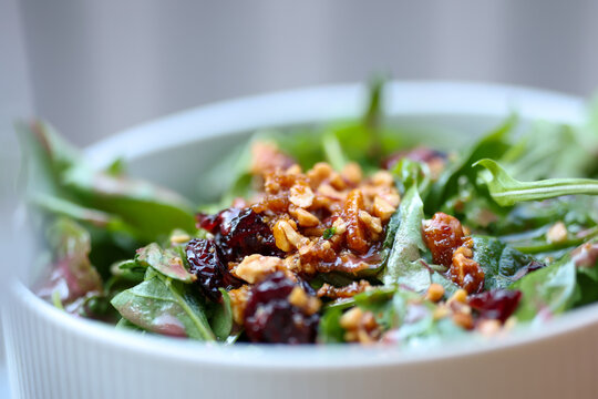 Fresh greens topped with chopped nuts and dried cranberries in a white bowl, showcasing color and texture.