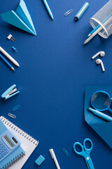 Naklejka premium Back to school blue stationery flat lay with supplies and workspace on solid vertical blue background with empty space in the middle