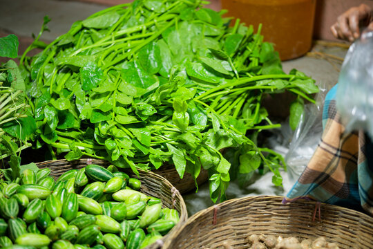 Fresh green leafy vegetables and pointed gourds in woven baskets at a local market stall