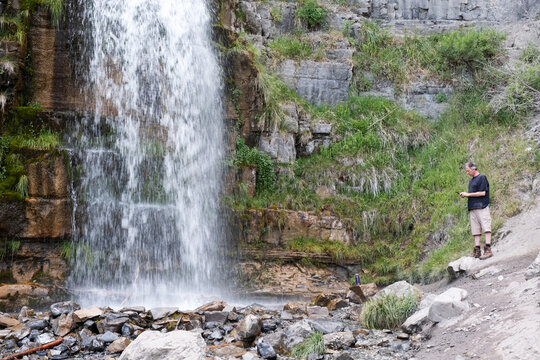 Man looks at phone instead of beautiful waterfall in front of him at Stewart Falls near Sundance, UT. Distractions of technology.  Caucasian man on nature hike staring at mobile phone.