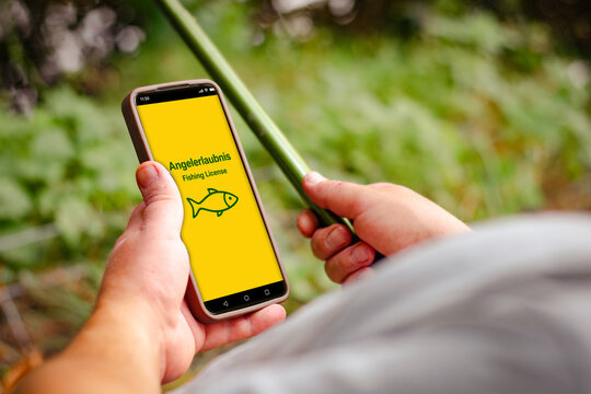 Digital fishing permit displayed on smartphone held by person with fishing rod, green foliage in background, showcasing modern fishing regulations and technology