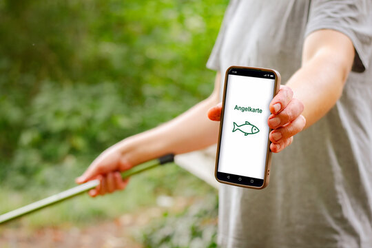 Digital fishing permit displayed on smartphone held by a person outdoors, with a fishing rod visible in the background among greenery and natural surroundings