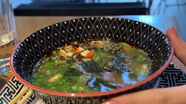 Traditional miso soup with tofu and seaweed in black bowl, authentic Japanese restaurant dish served hot with elegant table presentation