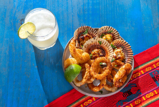 Peruvian hot seafood appetizers platter with parmesan scallops, fried calamari and Pisco Sour drink