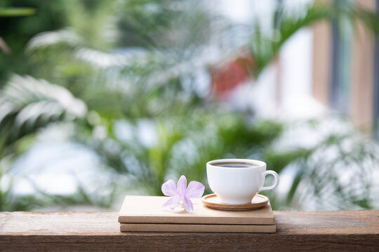White ceramic cup and purple orchid flower on stack of notebook