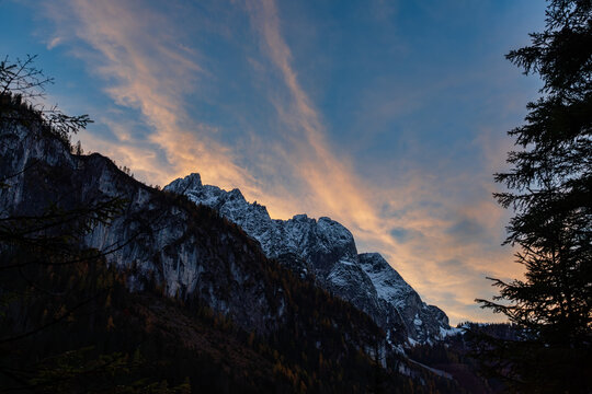  The alpine landscape with snowy towering mountains peaks against dramatic clouds glowing with golden hues during sunset.Located in the Gosau Valley in Upper Austria.