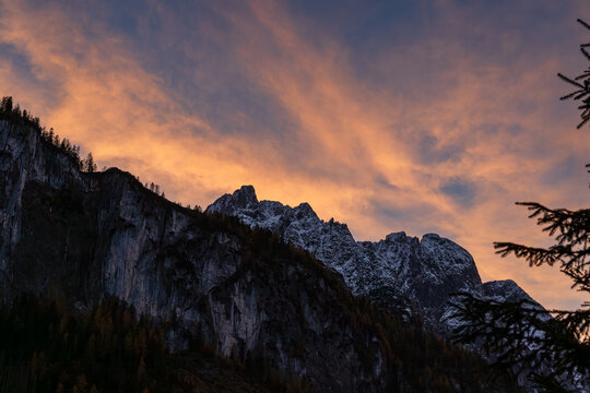 The snowy towering mountain peaks beneath dramatic clouds glowing with golden hues during a beautiful sunset. Located in the Gosau Valley in Upper Austria.