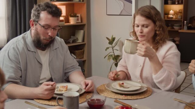 Multigenerational Caucasian family eating dessert and drinking tea at dining table, talking. Ideal for promoting family-oriented products, food brands, and domestic lifestyle services