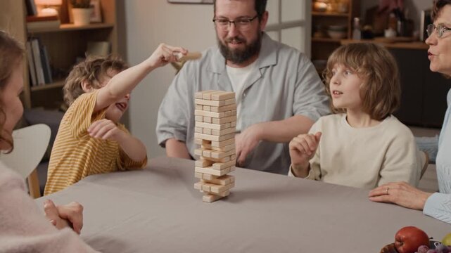 Caucasian family with middle aged parents and two young boys playing wooden block tower game at table. Clip for advertising family board games, home entertainment, and quality time