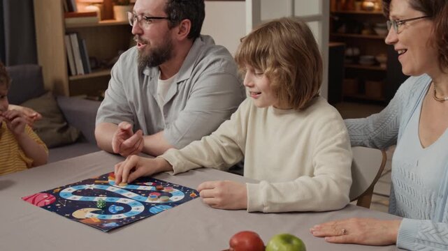 Caucasian family with young father, senior grandmother and two young kids playing space board game at home table, rolling dice and celebrating. Clip for family insurance or home entertainment ads