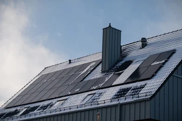 House roof equipped with photovoltaic solar panels partially covered in snow on a bright winter day.  © snapshotfreddy