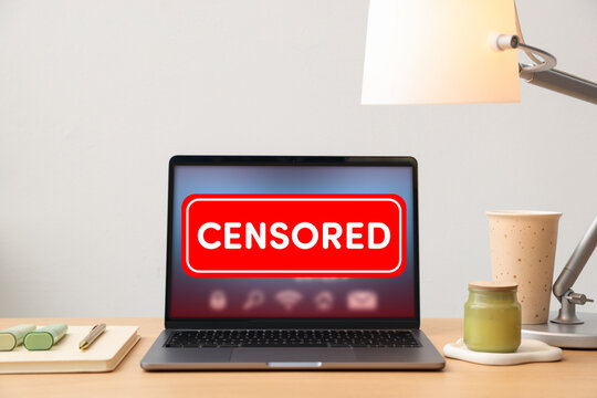Laptop displaying censored content on desk. Information filtering