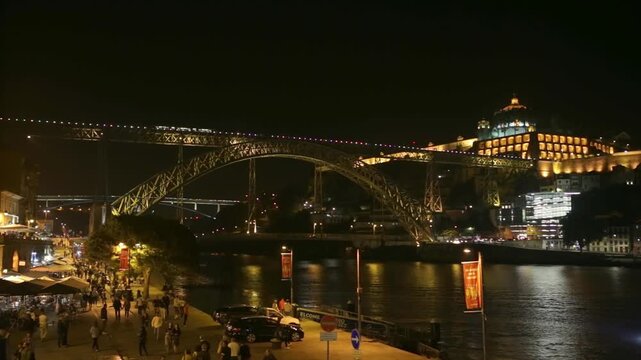 Magnificent night view of the illuminated dom luis i bridge and serra do pilar monastery over the douro river, with tourists walking along the bustling riverside promenade in porto, portugal
