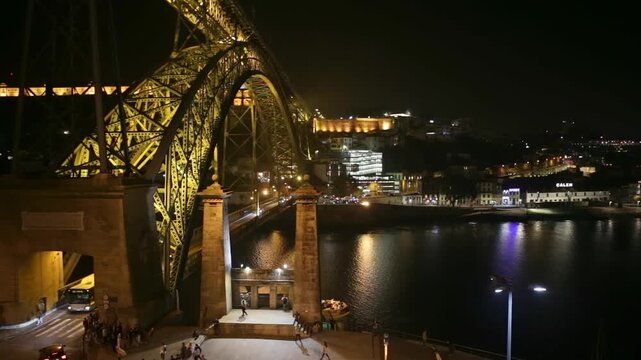 Majestic dom luis i bridge brilliantly illuminated against the dark night sky, with bustling traffic and pedestrians crossing over the serene douro river in the vibrant city of porto, portugal