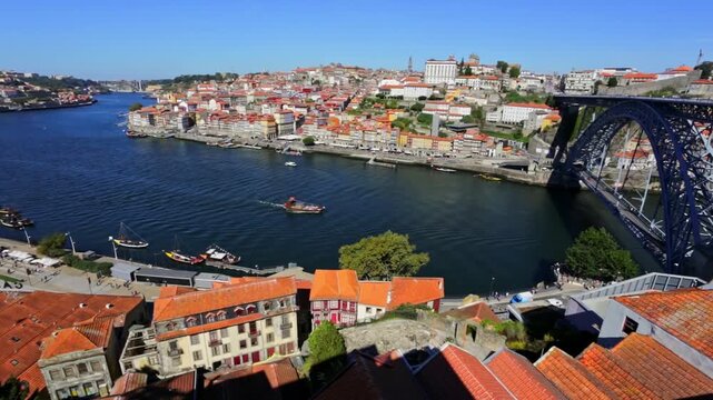 Picturesque aerial view of the historic ribeira district in porto, portugal, showcasing the iconic dom luis i bridge and traditional rabelo boats navigating the scenic douro river on a sunny day