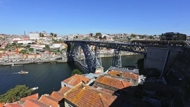Sunny day illuminating the iconic dom luis i bridge, a double deck metal arch bridge, as a metro train crosses its upper deck over the beautiful douro river in the historic city of porto