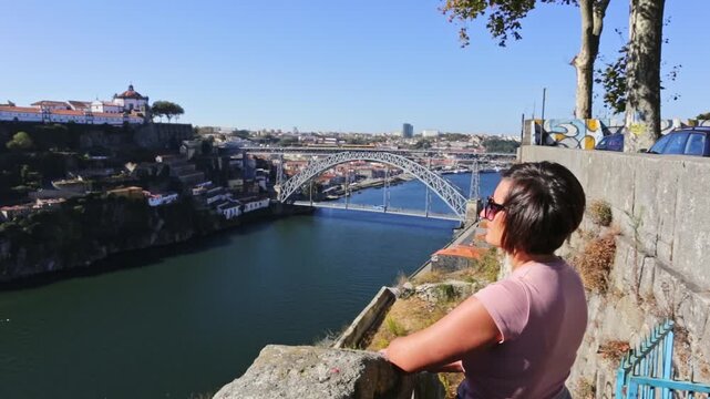 Young female tourist enjoying the panoramic view of the historic city of porto and the douro river, with the iconic dom luis i bridge standing out against a clear blue sky on a sunny day