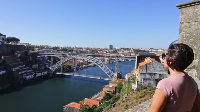 Woman looking at the douro river and the iconic dom luis i bridge, a major landmark of porto, portugal, on a bright sunny day, with the historic ribeira district visible in the background