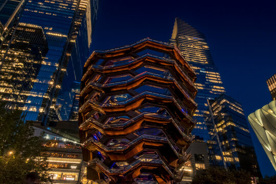 New York, NY - US - Jul 20, 2026 Twilight view of the Vessel at Hudson Yards glowing in warm tones, framed by sleek glass skyscrapers and deep blue sky, capturing New York City&rsquo;s modern skyline.