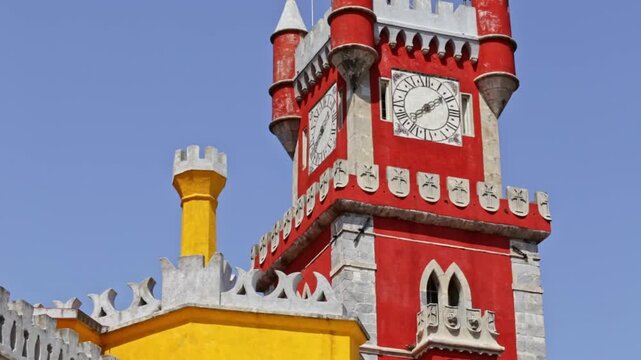 Majestic red and yellow clock tower of the palacio da pena in sintra, portugal, standing against a clear blue sky on a sunny day. Romanticist architecture and a famous unesco world heritage site