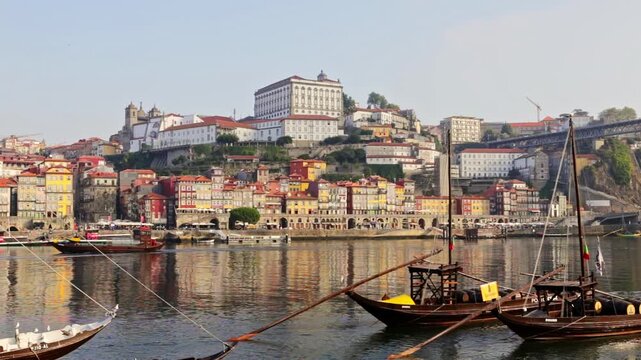Historical rabelo boats, once used for transporting port wine, floating on the douro river with the colorful ribeira district and the dom luis i bridge in the background on a sunny day