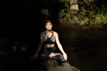 Fotobehang Lotusbloem Woman practicing yoga in Indian nature near flowing river landscape, showing meditation, lotus pose, sunlight, outdoor wellness practice and traditional yoga lifestyle surrounded by peaceful scenery..  © Anton