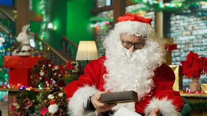 Fototapeta premium Santa Claus catches a gift box falling from above while reading children's letters as the present lands in his lap in a Christmas miracle scene.