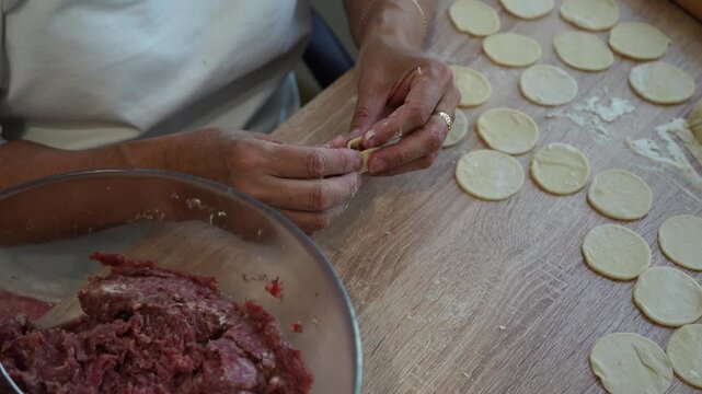 Traditional homemade dumpling preparation with hands placing meat filling on dough circles during cooking process