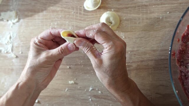 Hands preparing handmade dumplings by shaping dough and filling on a wooden table, showing traditional homemade cooking techniques and food preparation