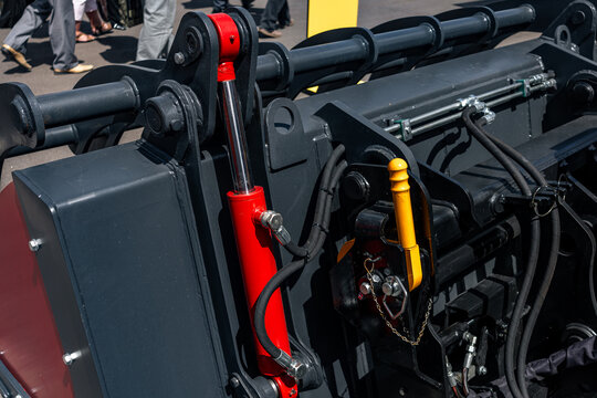 Skid steer loader attachment quick coupler with locking lever. Modern compact construction machinery hydraulic cylinder mechanism with hoses on grey frame and vehicle technical details.