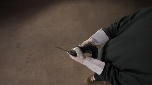 High angle view gardener wearing protective work gloves using a handheld electric hedge trimmer, demonstrating professional landscaping and garden maintenance