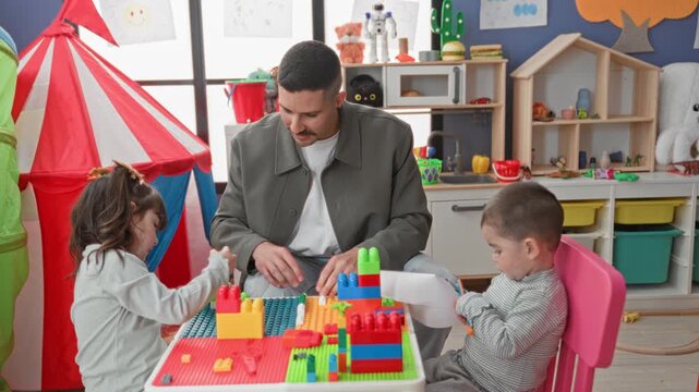 Man helps two children place colorful toy blocks with hands on table in building; nurturing learning.