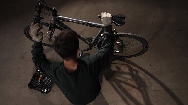 High angle view mechanic lying on the ground repairing a bicycle using hand tools from a kit, focusing on the bike's drivetrain and suspension for proper function and safety