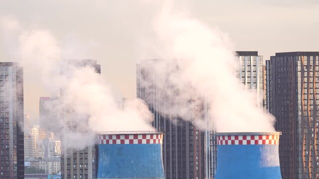 Urban industrial facility with chimneys releasing steam beside high rise buildings showing energy infrastructure and city development