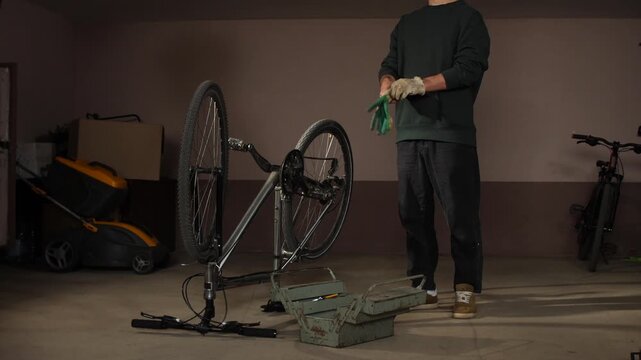 Man wearing work gloves preparing to repair an upside down bicycle using tools from a metal toolbox, performing maintenance in a home garage