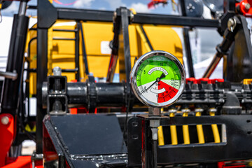 Fototapeta premium Agricultural sprayer fluid pressure gauge manometer dial closeup. Modern farm machinery liquid distribution section on black chassis frame with yellow water tank and equipment technical details.