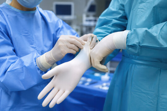 Sterile surgical nurse assists a surgeon in putting on sterile gloves in a modern hospital operating room, ensuring strict hygiene protocols are followed before a medical procedure begins.