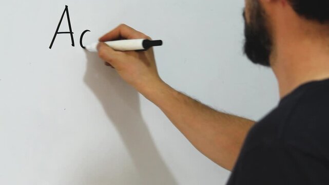 Detailed view of a man writing capital and small letters of the latin alphabet on an acrylic whiteboard