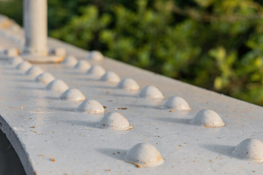 Row of domed rivets on the white painted steel plate of an old road bridge