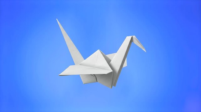 Traditional Japanese white folded paper origami crane bird isolated on a clean blue background. Symbolic asset representing peace, hope, travel, freedom, and handcrafted paper art.