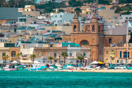 Marsaxlokk Malta Fishing Village: Traditional Colorful Luzzu Boats and Church at Waterfront | Turquoise Sea Harbor with Coastal Town Buildings | Telephoto Mediterranean Fishing Port