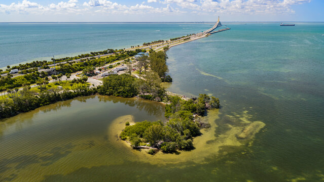 Aerial view from the north of Sunshine Skyway Bridge. I-275 crosses low-lying islands of Tampa Bay. A J-shaped fishing spit and colorful waters create a popular recreation area.