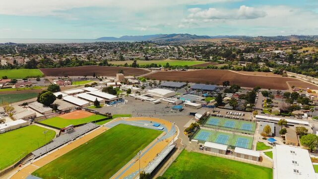 Low aerial drone pass over school athletic campus showing running track football field and bleachers