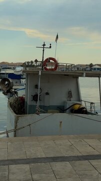 Vertical close-up aboard a traditional fishing boat in Marzamemi featuring ropes, fishing nets and the helm, highlighting Sicilian maritime craftsmanship.