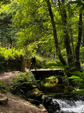 Hiker crossing stone bridge over stream on Camino de Santiago, Spain