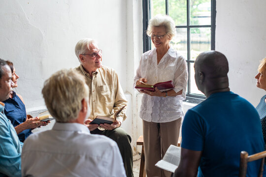 Diverse group of seniors in a discussion circle with books in hand.